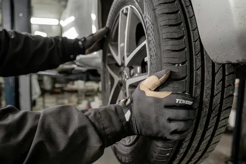 Hände in Arbeitshandschuhen prüfen die Lauffläche eines montierten Reifens
