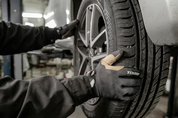 Hände in Arbeitshandschuhen prüfen die Lauffläche eines montierten Reifens